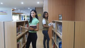 dua mahasiswi sedang membaca di perpustakaan UBM